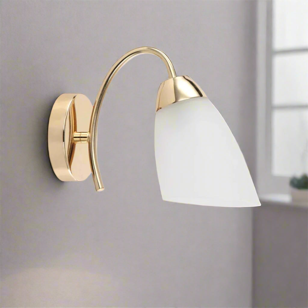 Wall-mounted light fixture with gold frame and white shade on a white background